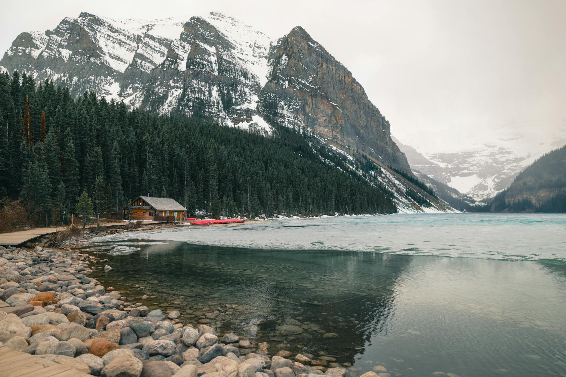 Serene view of Lake Louise with snow-capped mountains and a cozy cabin in Banff, Canada.
