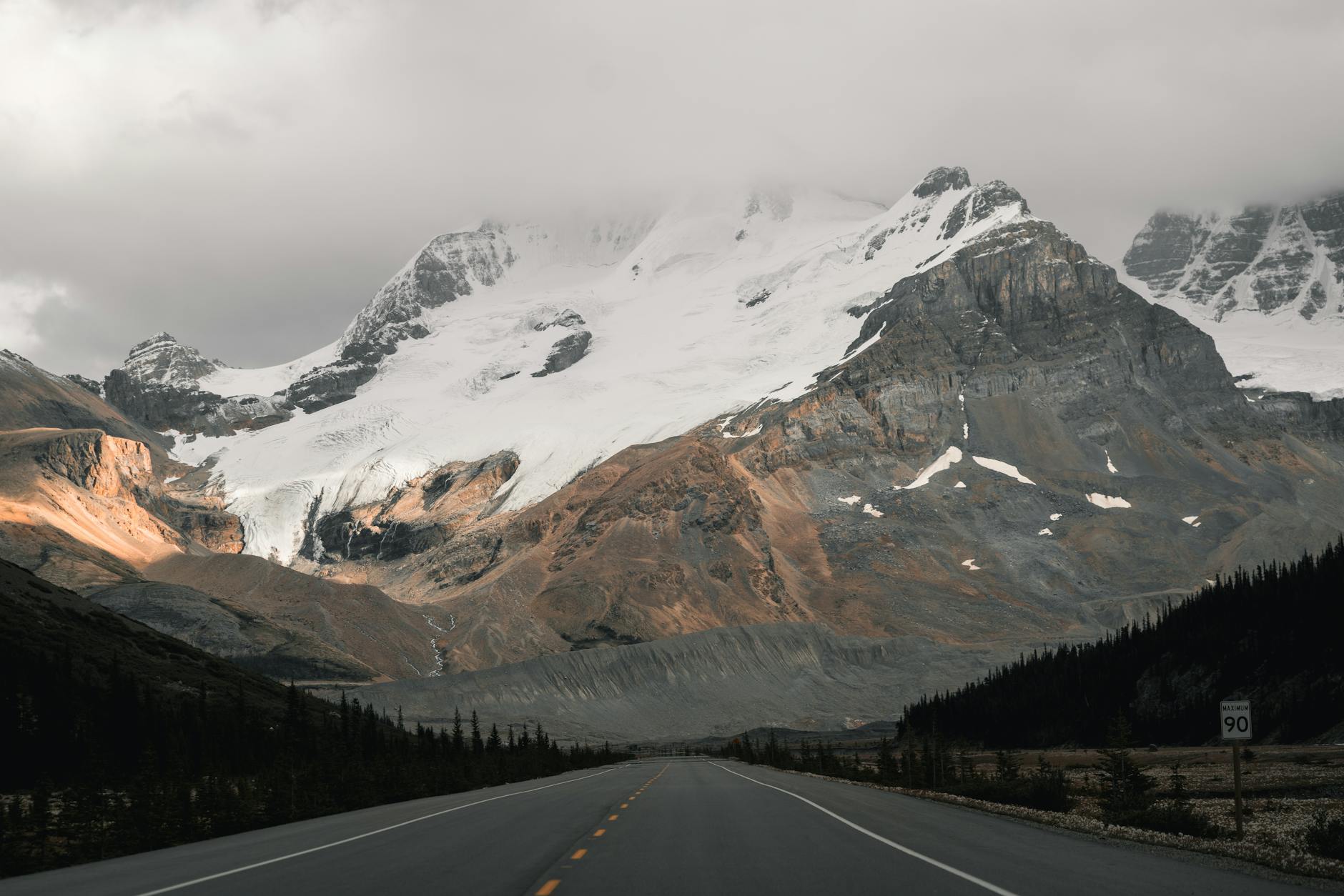 Breathtaking road view through Jasper, Alberta with stunning snow-capped mountains and dramatic skies.