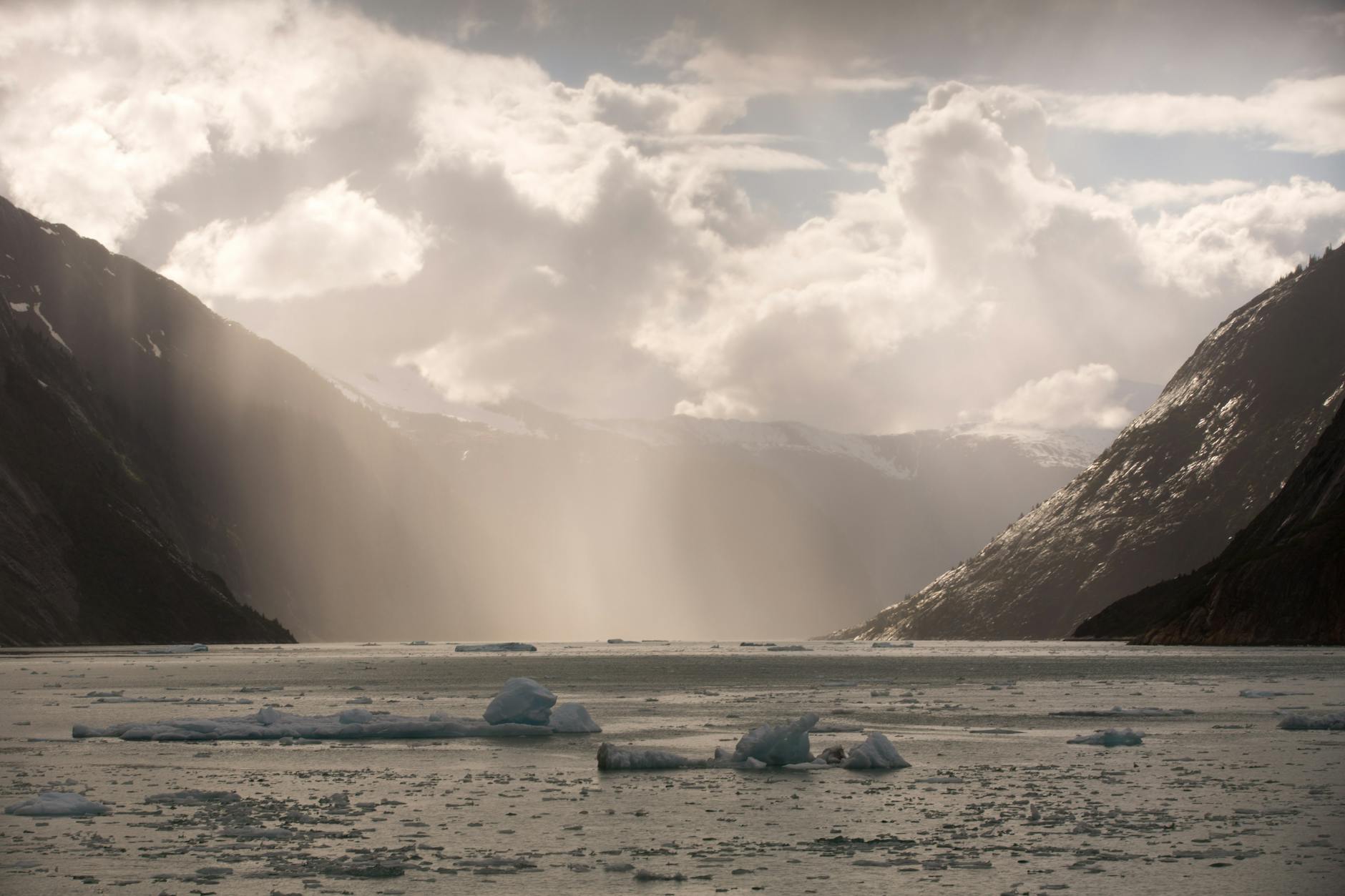 Glacier Bay Alaska fjord icebergs floating calm water dramatic mountains sunbeams
