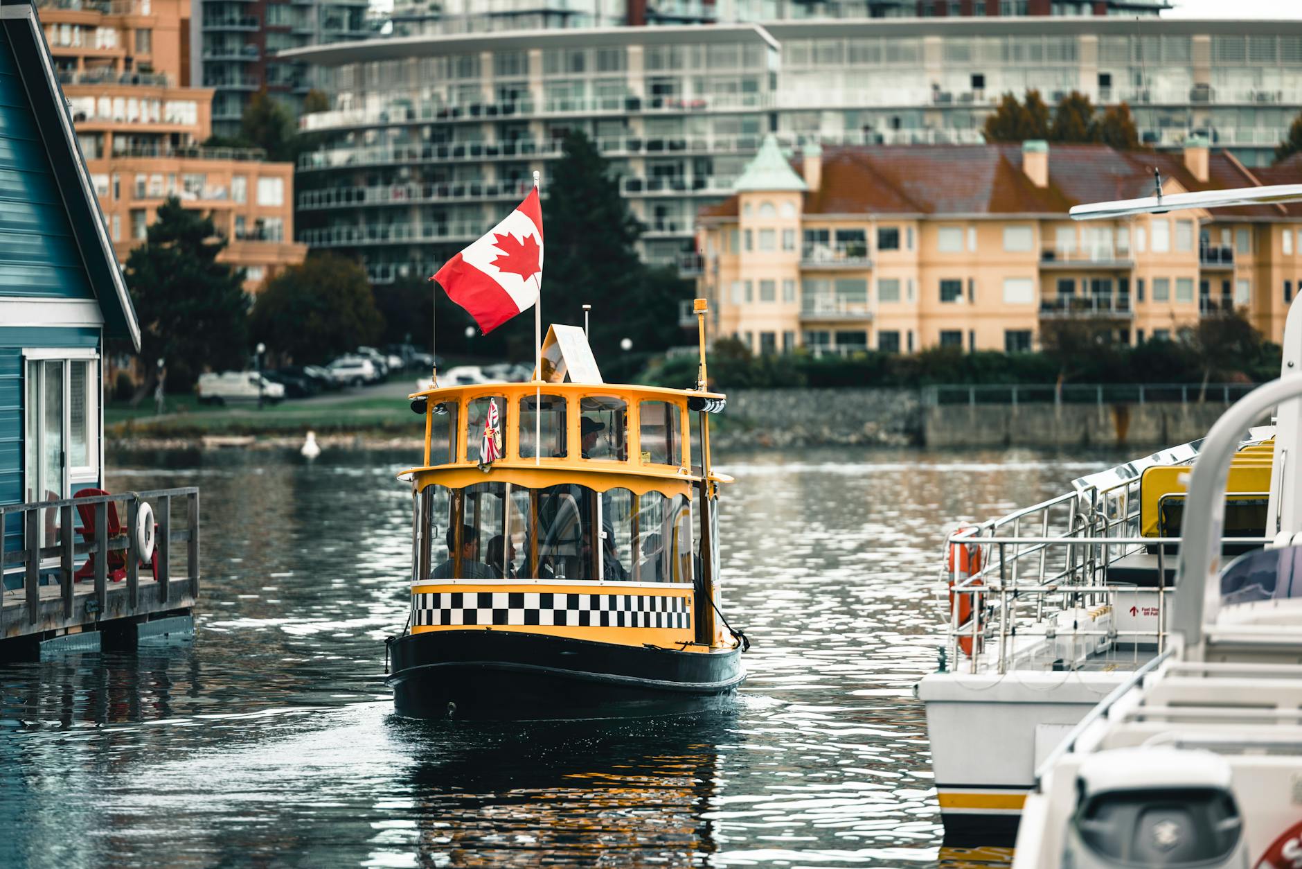 A charming yellow ferry with a Canadian flag navigates Victoria Harbour, British Columbia.